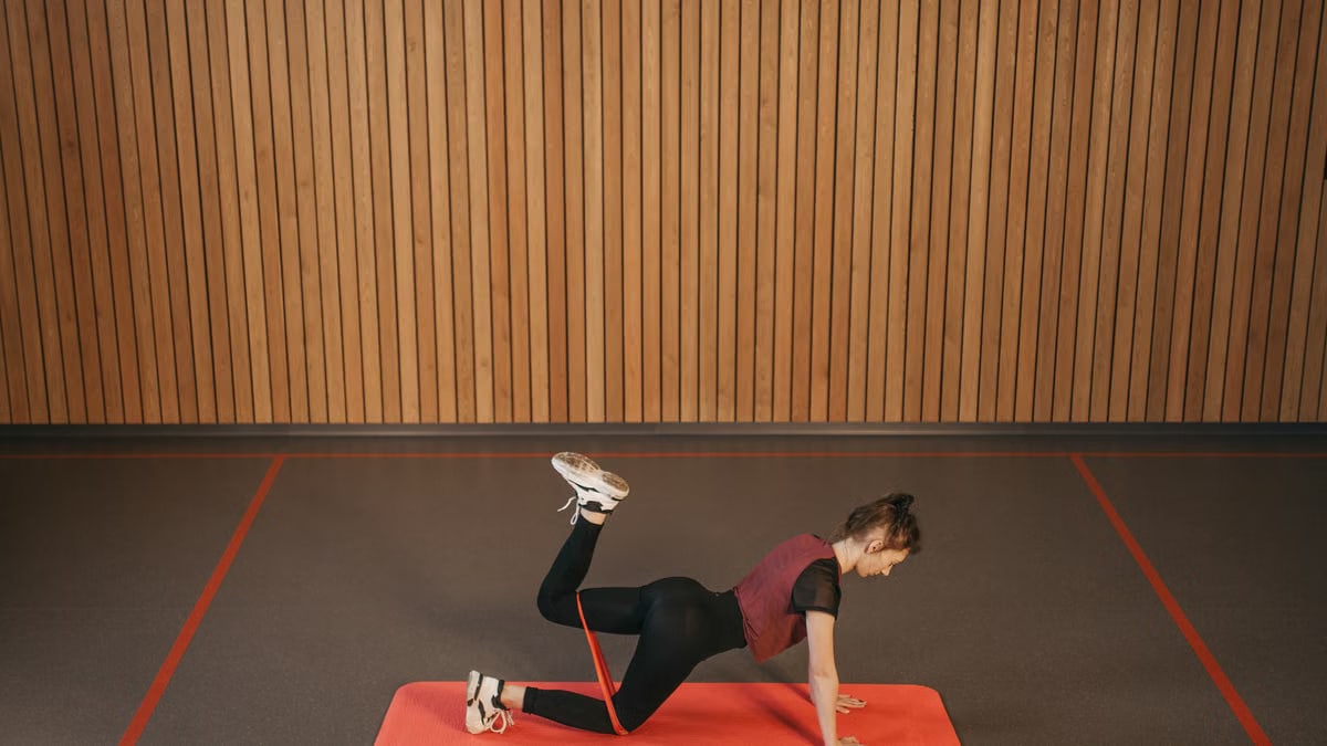 Woman performing a resistance band workout on a mat indoors, focusing on fitness and strength.